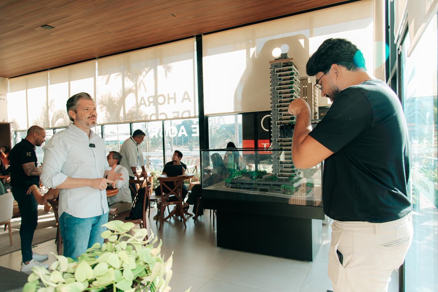 Cinegrafista gravando entrevista ao lado da maquete de um empreendimento imobiliário